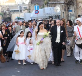 A bride and groom walk down the street with other people.